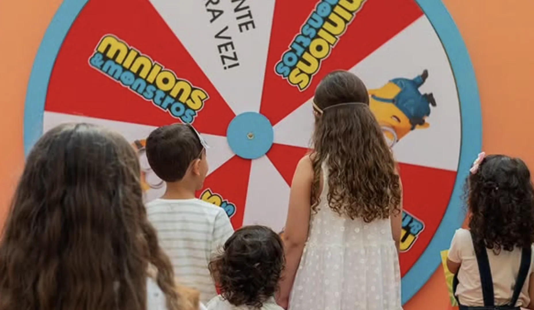 Crianças observam roleta que define o personagem na experiência Minions & Monstros.