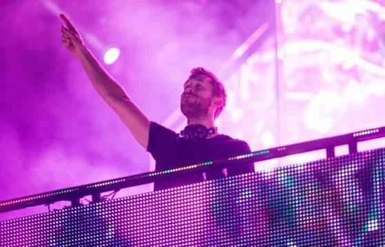 Calvin Harris durante apresentação no palco do Rock in Rio, com iluminação em tons de rosa e roxo.
