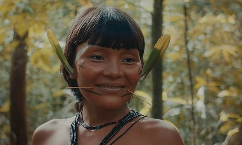 Mulher indígena Yanomami aparece sorrindo em meio à floresta em cena documental.