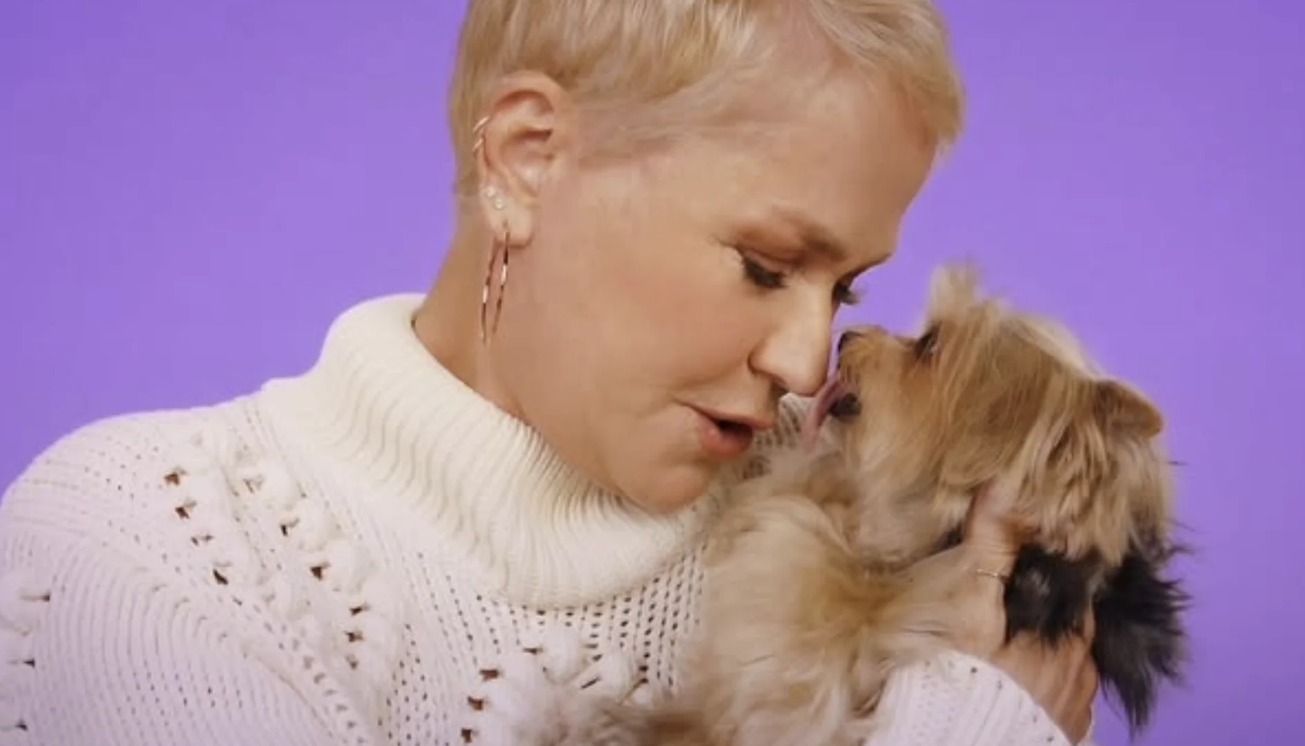 Xuxa segura um cachorro nos braços enquanto os dois encostam os rostos em um fundo lilás, representando a parceria da apresentadora com a Petlove.