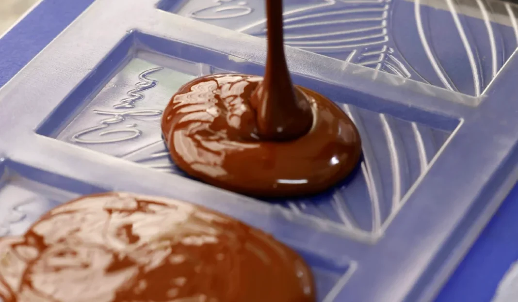 Chocolate derretido sendo colocado em formas para produção de barras artesanais.