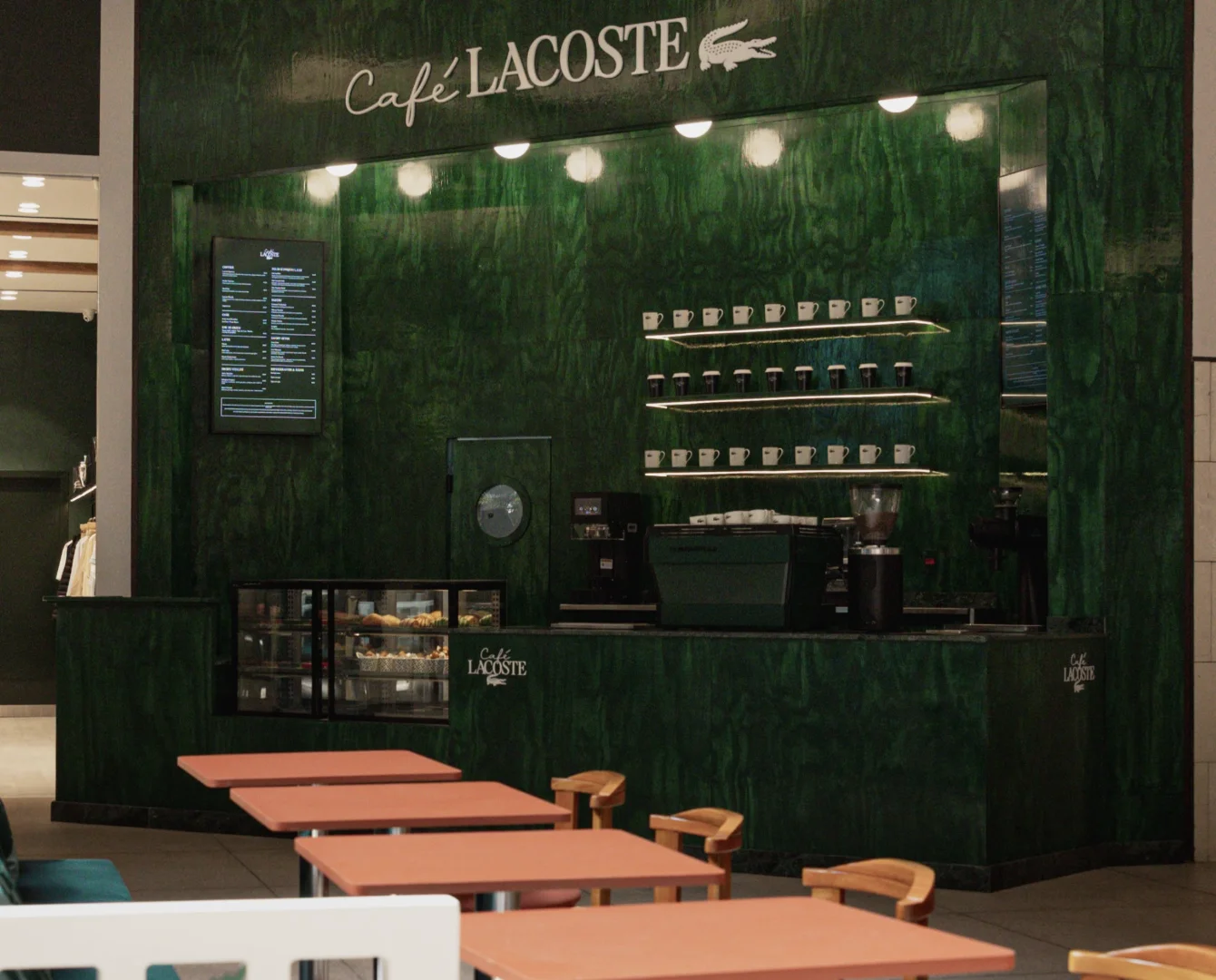 Fachada e balcão verde do Café Lacoste com mesas organizadas no salão.