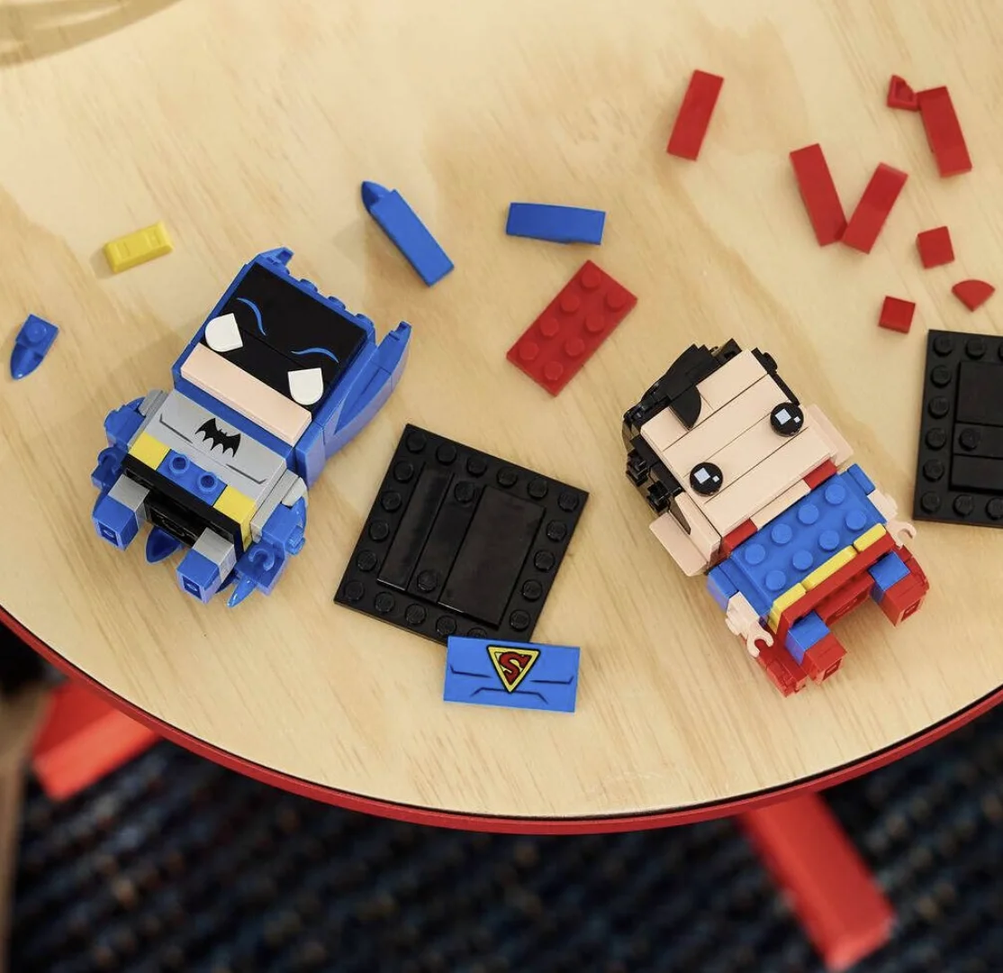 Peças dos BrickHeadz de Batman e Superman espalhadas sobre uma mesa durante a montagem.