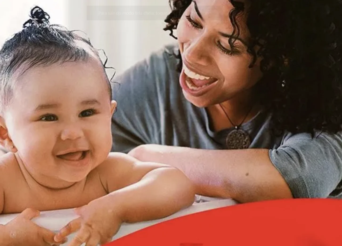 Bebê sorrindo durante o banho ao lado da mãe.
