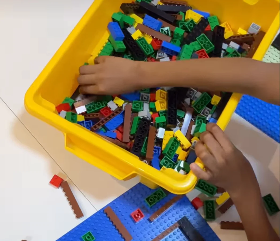 Criança escolhe peças coloridas de LEGO em caixa amarela.