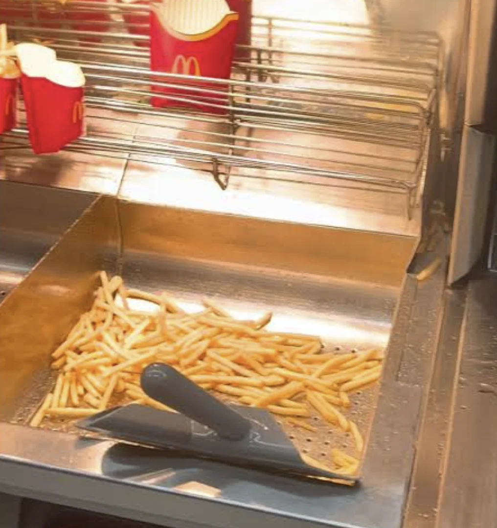 Batatas fritas na área de preparo de um restaurante McDonald’s, com embalagens vermelhas ao fundo.