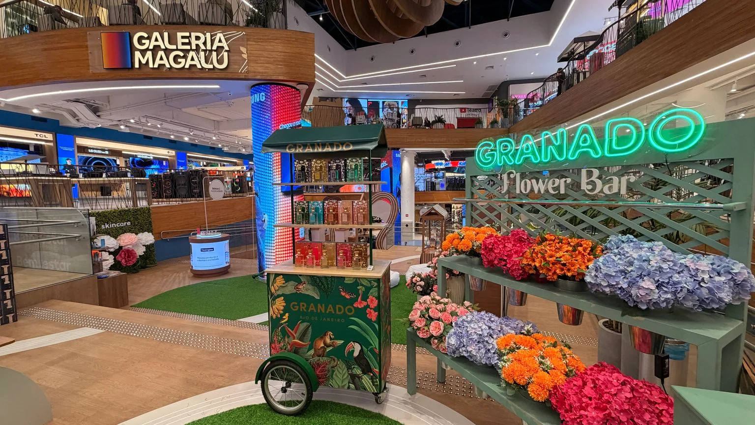 Flower Bar da Granado com flores coloridas e um carrinho de produtos na Galeria Magalu.