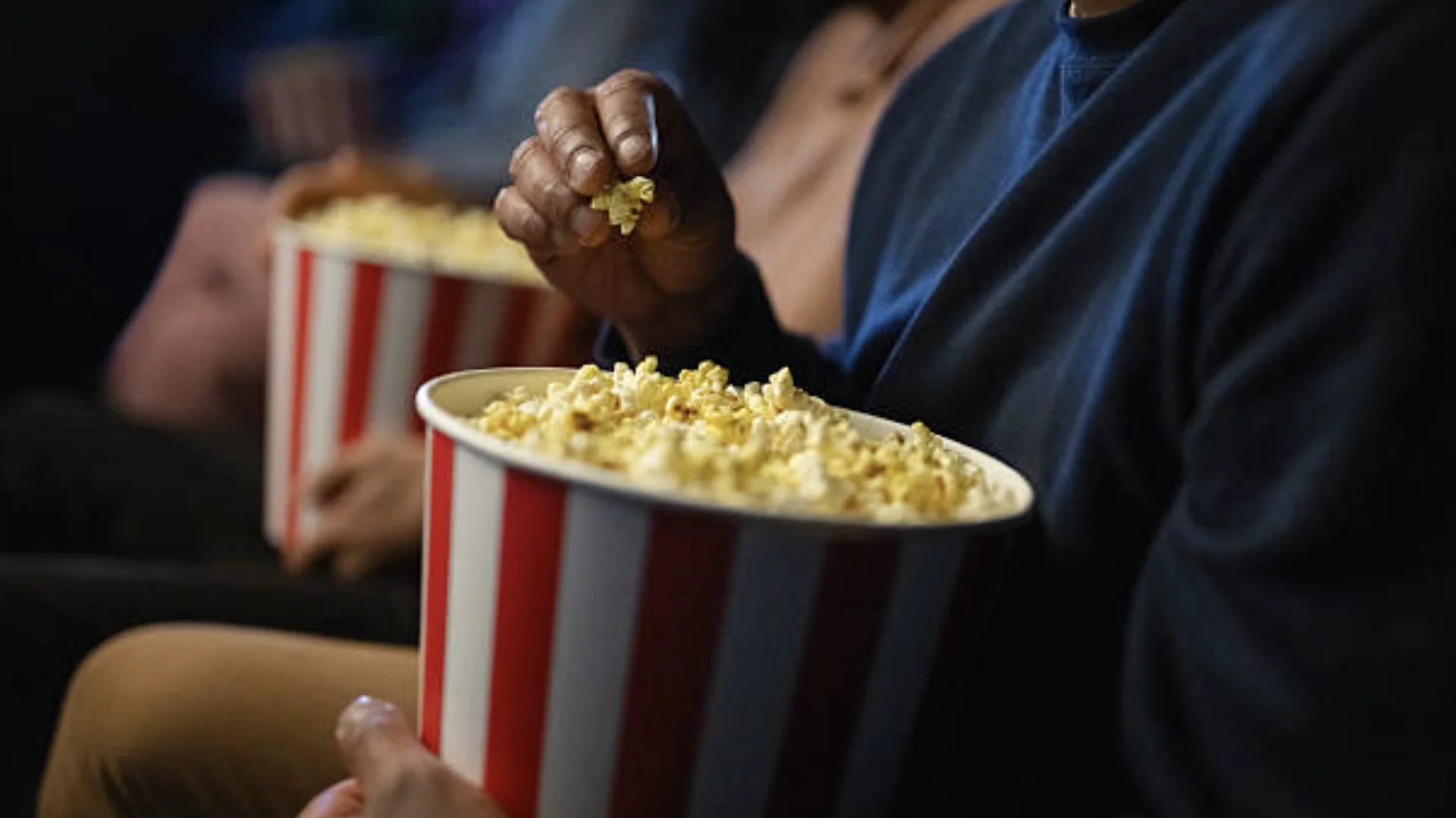 Pessoas comendo pipoca durante sessão de cinema.