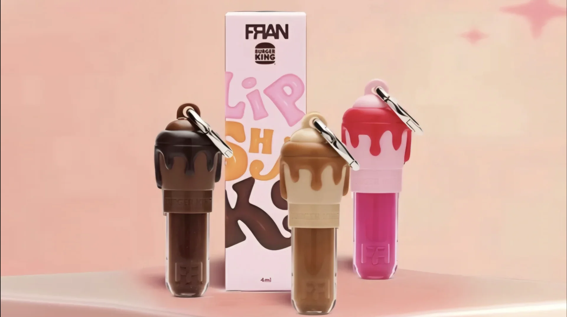 Três glosses LipShakes da parceria Burger King e Franciny Ehlke, com embalagem da coleção FRAN ao fundo.