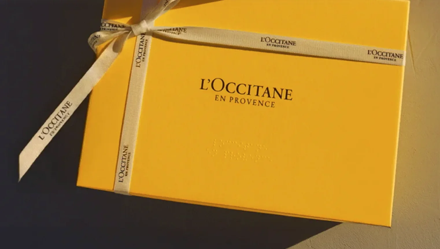 Caixa de presente amarela da L’Occitane en Provence com fita personalizada da marca.