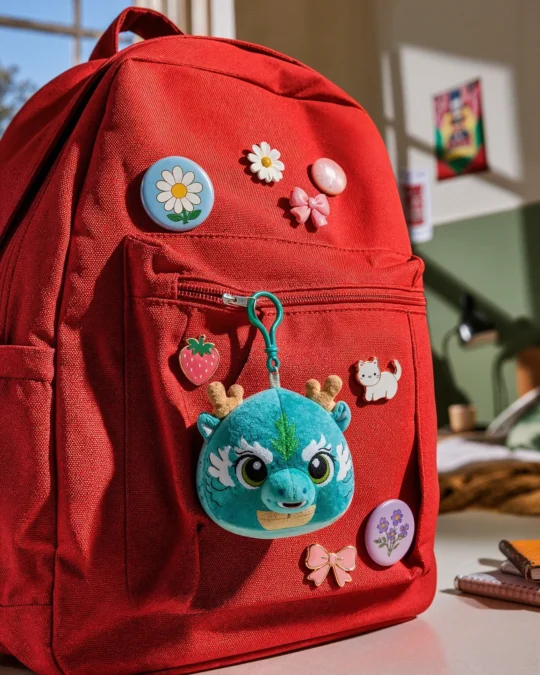 Pelúcia Dragão Azul do China in Box pendurada em mochila vermelha com acessórios decorativos.