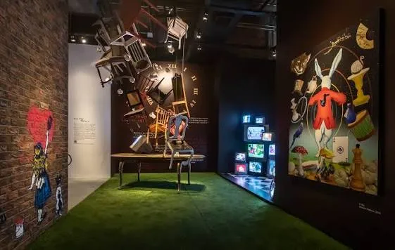 Ambiente da exposição Alice no País das Maravilhas com instalações artísticas e projeções.