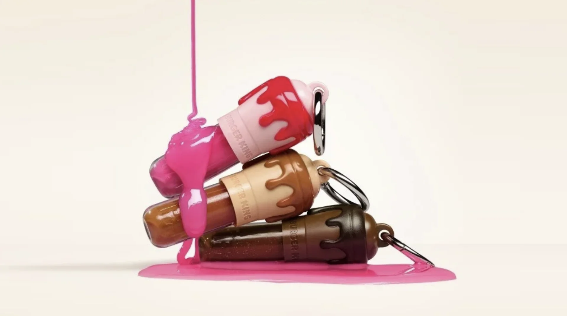 Três glosses Burger King e Franciny Ehlke em formato de chaveiro, nas cores rosa, caramelo e marrom.