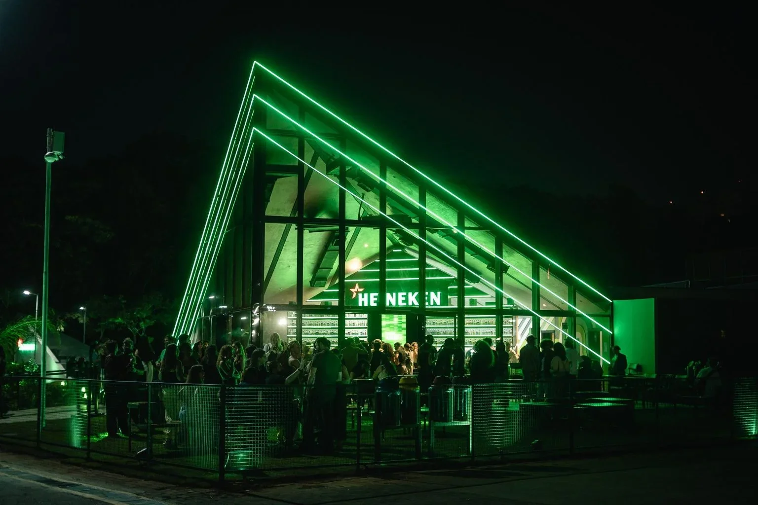 Fachada iluminada em verde da Heineken House durante evento noturno com visitantes.