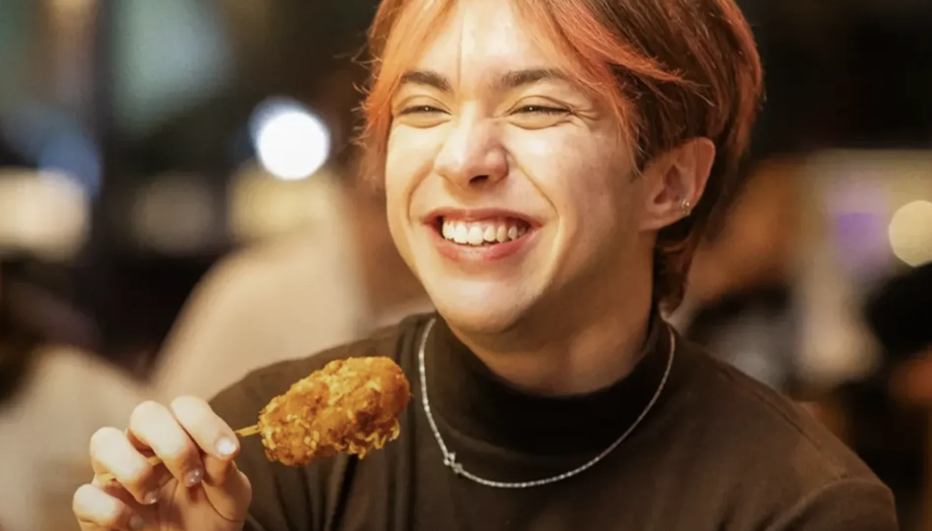 Pessoa sorridente segura um alimento empanado no palito durante experiência gastronômica do Outbac-K.