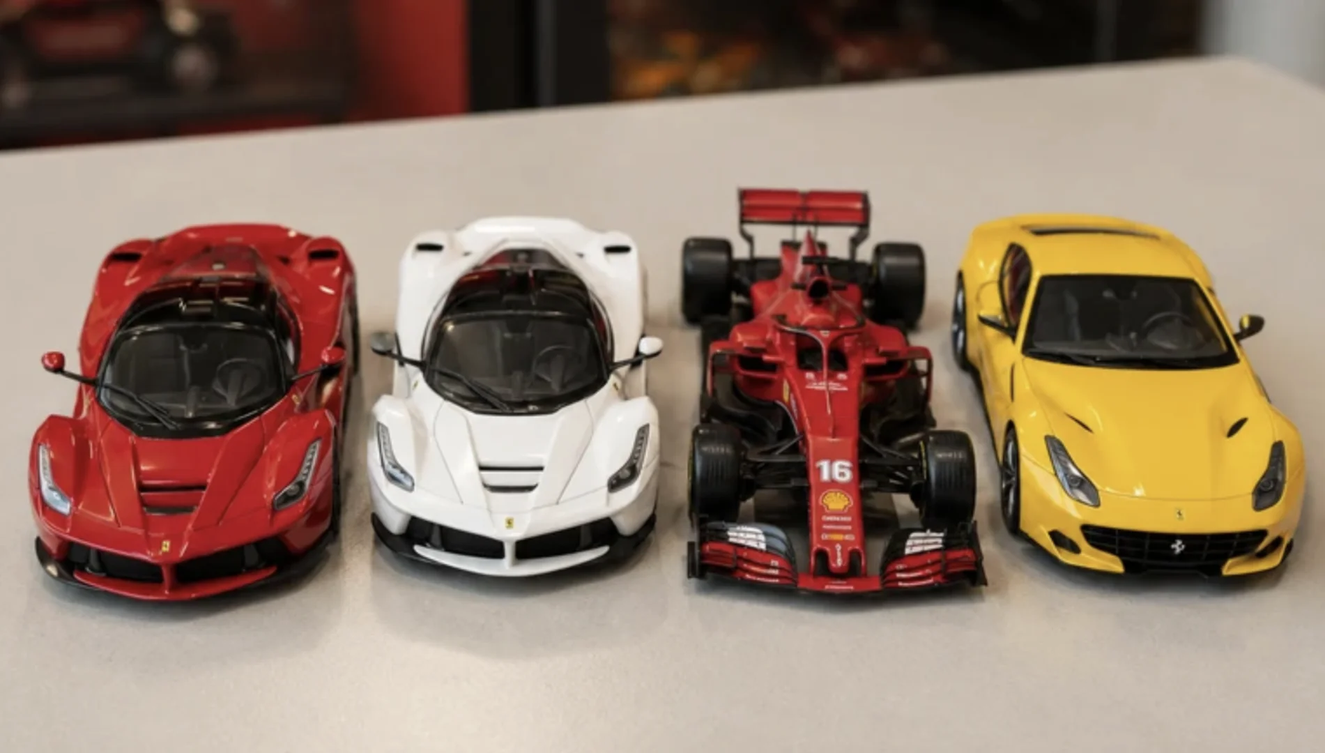 Quatro miniaturas Ferrari nas cores vermelha, branca e amarela, incluindo um carro de Fórmula 1.