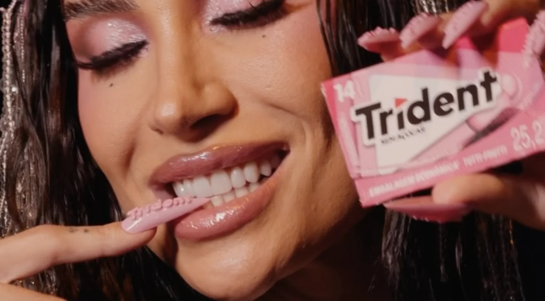 Boca Rosa exibe unha rosa feita de chiclete durante ação da Trident, segurando uma embalagem da marca próxima ao rosto.